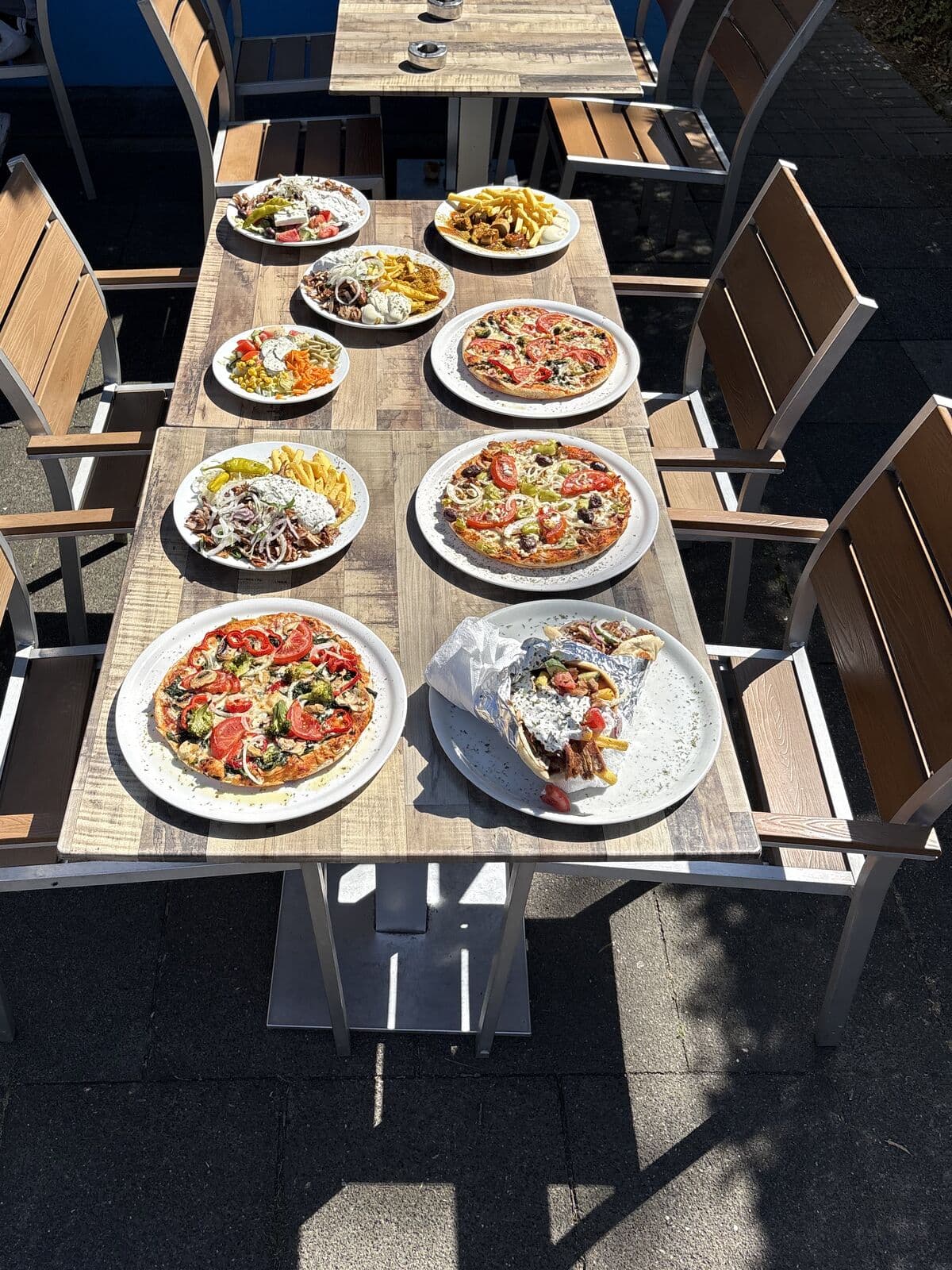 Gedeckte Tafel mit Gyros, Pizza, Salaten und Currywurst auf der Terrasse